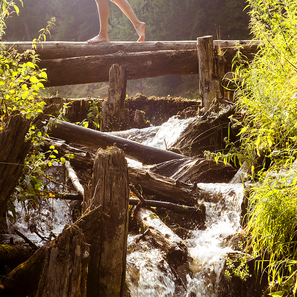 Legs of Caucasian woman walking on log crossing waterfalls