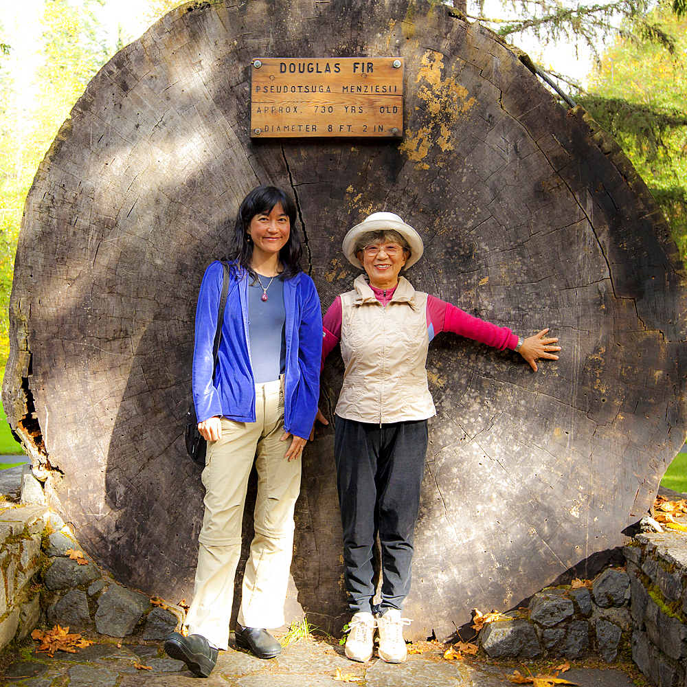 Smiling Japanese mother and daughter posing at tree stump