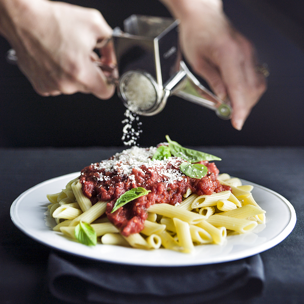 Hands grating parmesan cheese on penne pasta