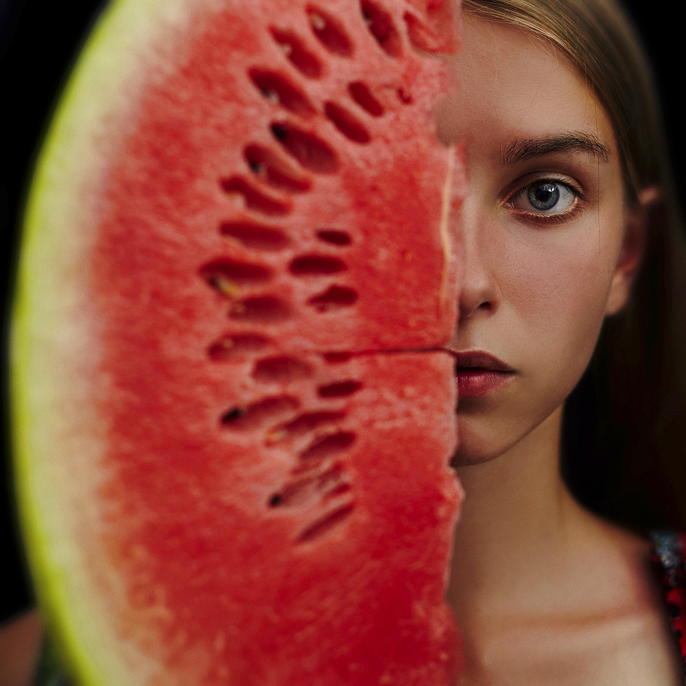 Caucasian girl holding slice of watermelon over half of face