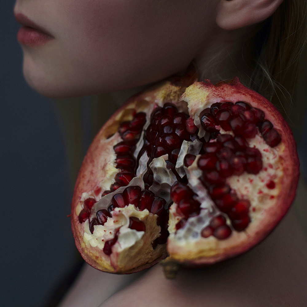 Caucasian girl balancing pomegranate slice on shoulder