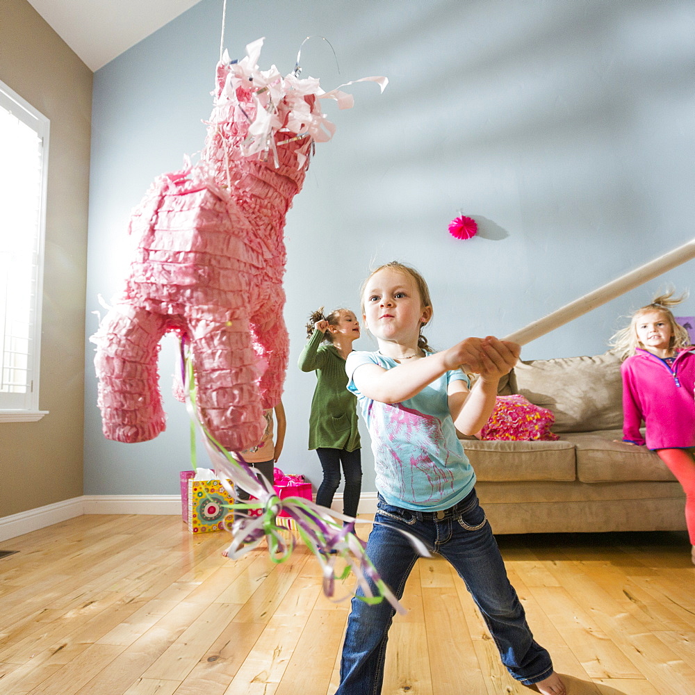 Caucasian girl hitting pinata at party