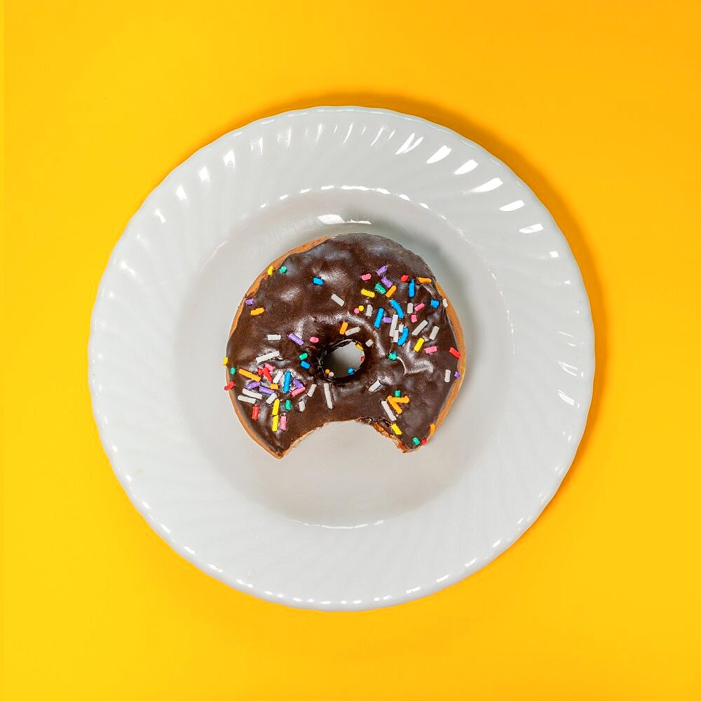 Overhead view of eaten donut with chocolate icing and sprinkles on white plate