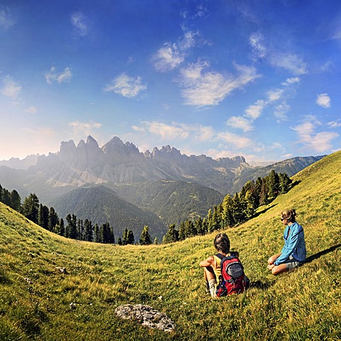 Hikers relaxing in a meadow enjoying the view of the Geisler group, Aferer Geisler mountains, Villnoesstal valley, province of Bolzano-Bozen, Italy, Europe