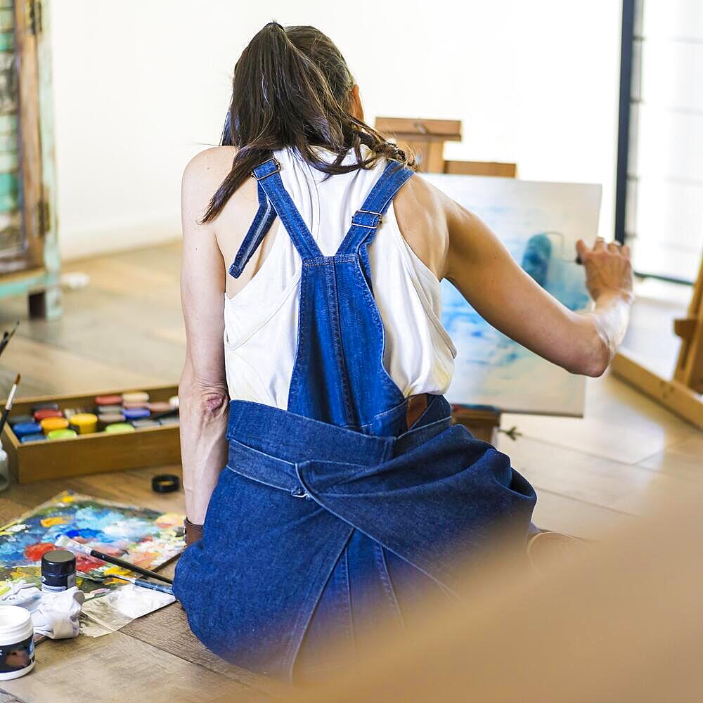 Woman artist painting on a canvas a blue abstract painting. Creative ywoman working on the floor in her art studio