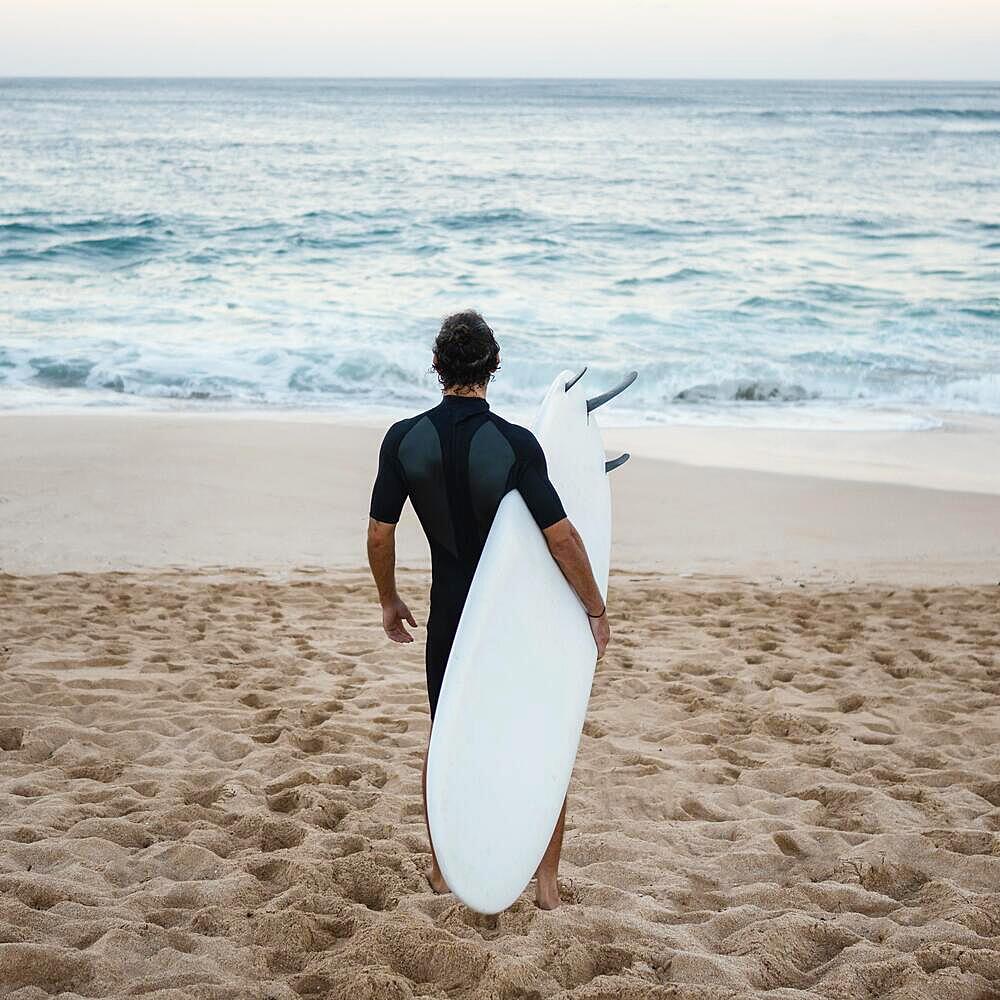 Man wearing surfer clothes walking sand from