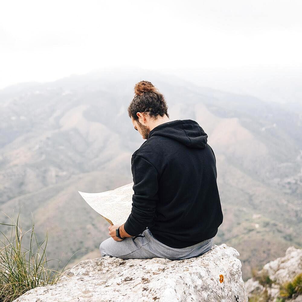 Male hiker sitting top rock looking map