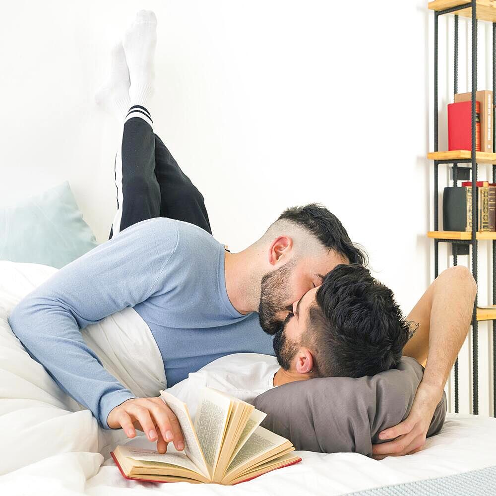 Man kissing his boyfriend lying bed with le s leaning wall