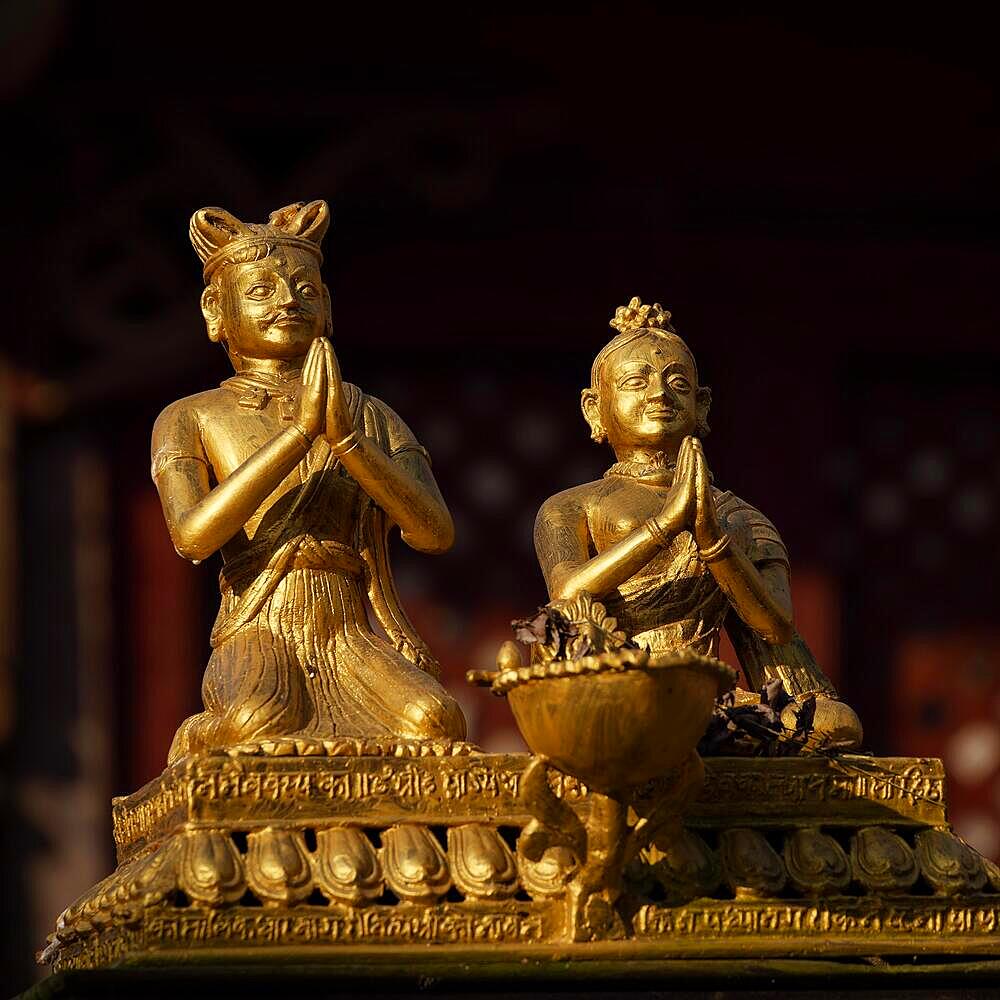 Golden statues of a man and a woman sitting and praying in the morning light, Bandipur, Nepal, Asia