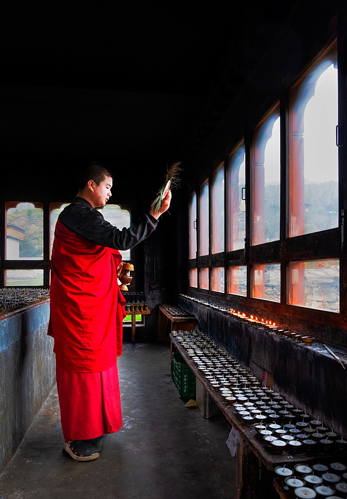 Portrait, Bhutanese Buddhist monk lights candles for worshippers to pray, Tamzhing Monastery, Bumthang District, Bhutan, Asia