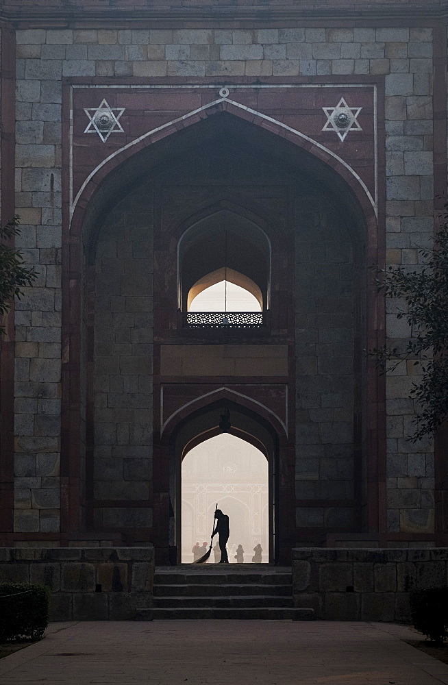 Silhouette of man sweeping under arch of Humayun's Tomb in Delhi, India, Asia