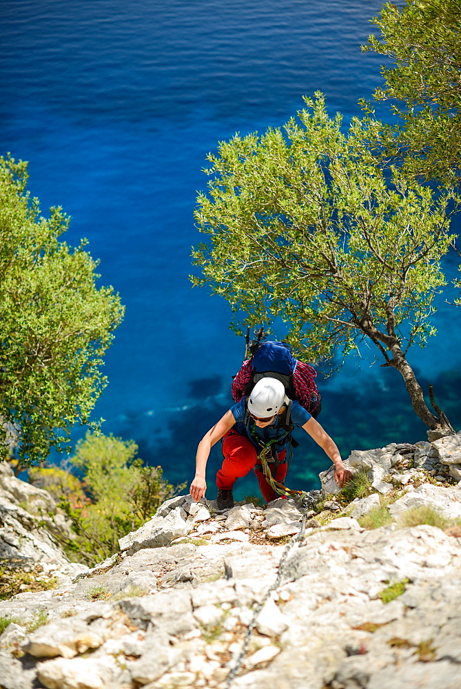 A young woman climbing a steep wall above the sea, secured with a chain, Golfo di Orosei, Selvaggio Blu, Sardinia, Italy, Europe