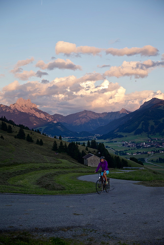 Young woman riding her bike near mountains at sunset, Rote Flueh, Gimpel, Hochwiesler, Tannheimer Tal, Tyrol, Austria