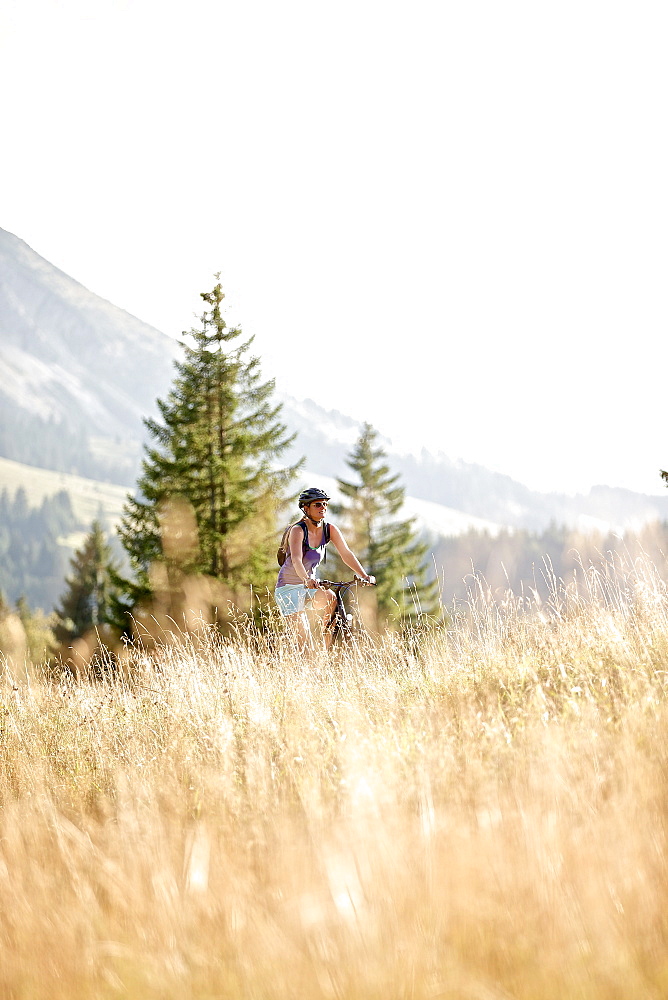 Young woman riding her bike near a meadow on a sunny day, Tannheimer Tal, Tyrol, Austria