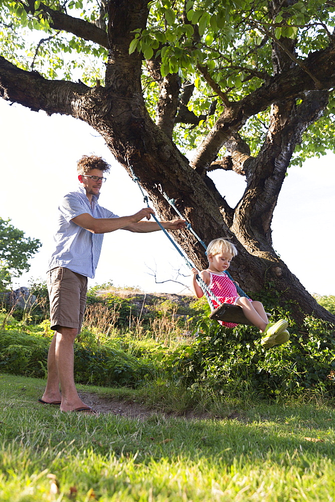 Father pushing young daughter on the swing, Summer, Baltic sea, MR, Bornholm, Svaneke, Denmark, Europe