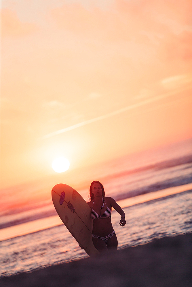 Female surfer goes with surfboard on the beach in sunset, surfing, Portugal, sunset