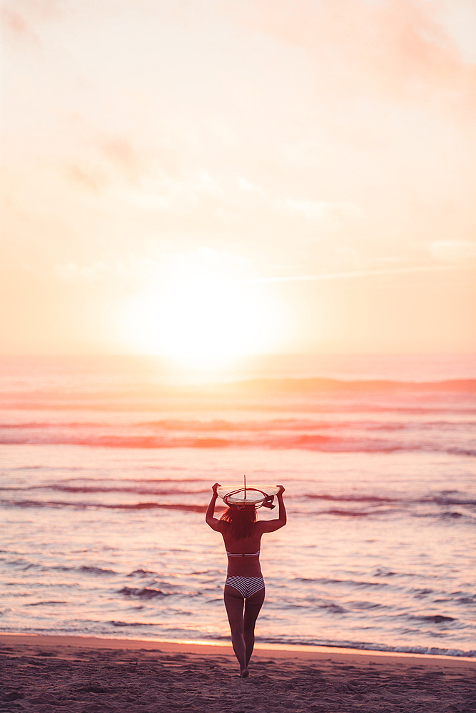 Female surfer goes with surfboard on the beach in sunset, surfing, Portugal, sunset