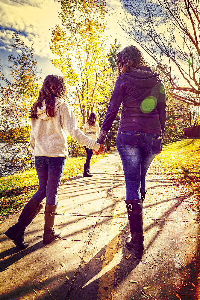 A mother and her two daughters walking and talking on a pathway in a city park on a warm autumn day, Edmonton, Alberta, Canada