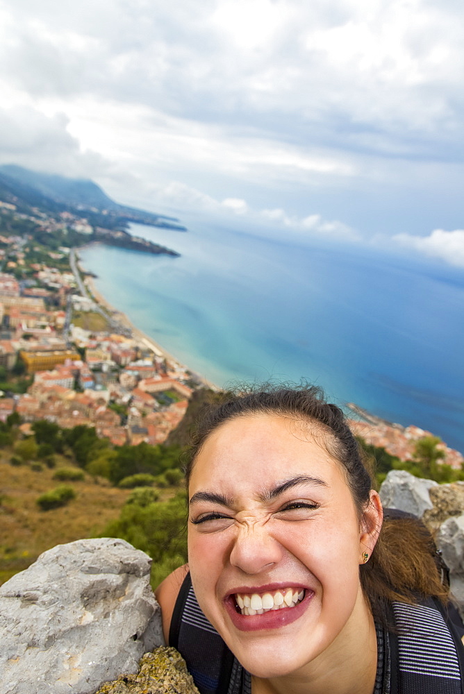 A young female tourist stands on a lookout above the Mediterranean coast, Cefalu, Sicily, Italy