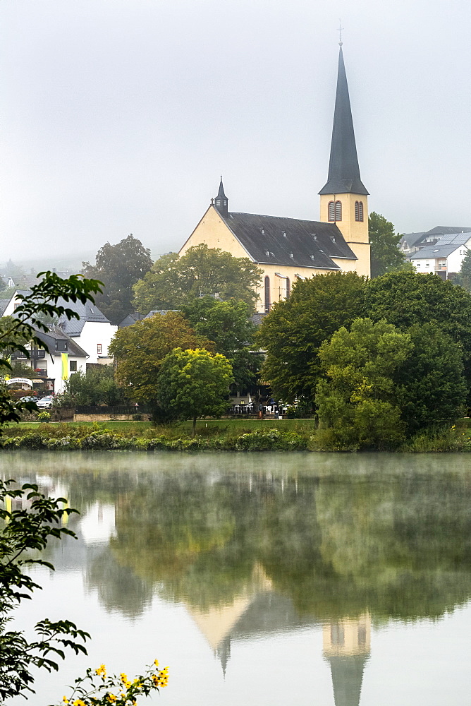 Misty river valley with church in treed area reflecting in the river, Krov, Germany