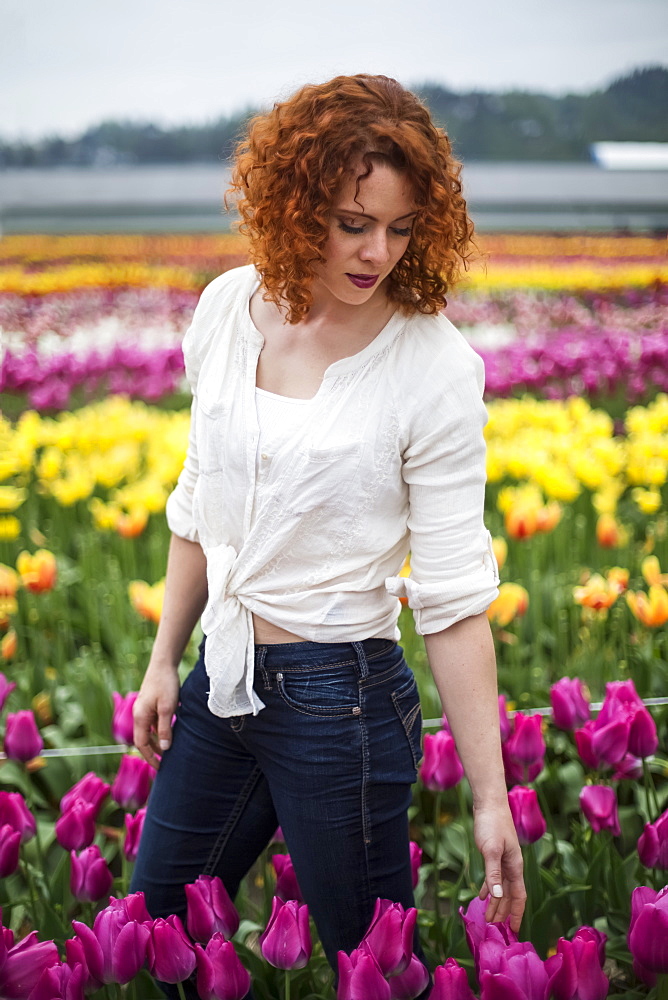 A woman with red hair stands in a field of tulips, Abbotsford, British Columbia, Canada