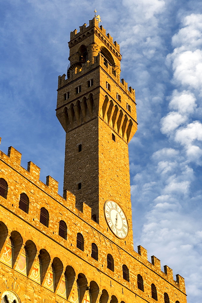 Large stone clock tower on top of castle walls with dramatic clouds and blue sky, Florence, Tuscany, Italy