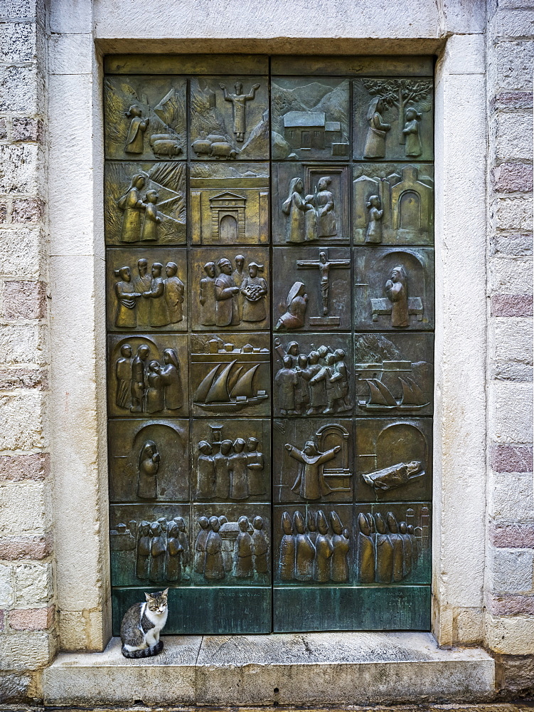 A metal door with pictograms placed in squares over the surface, and a cat sitting on the step, Montenegro