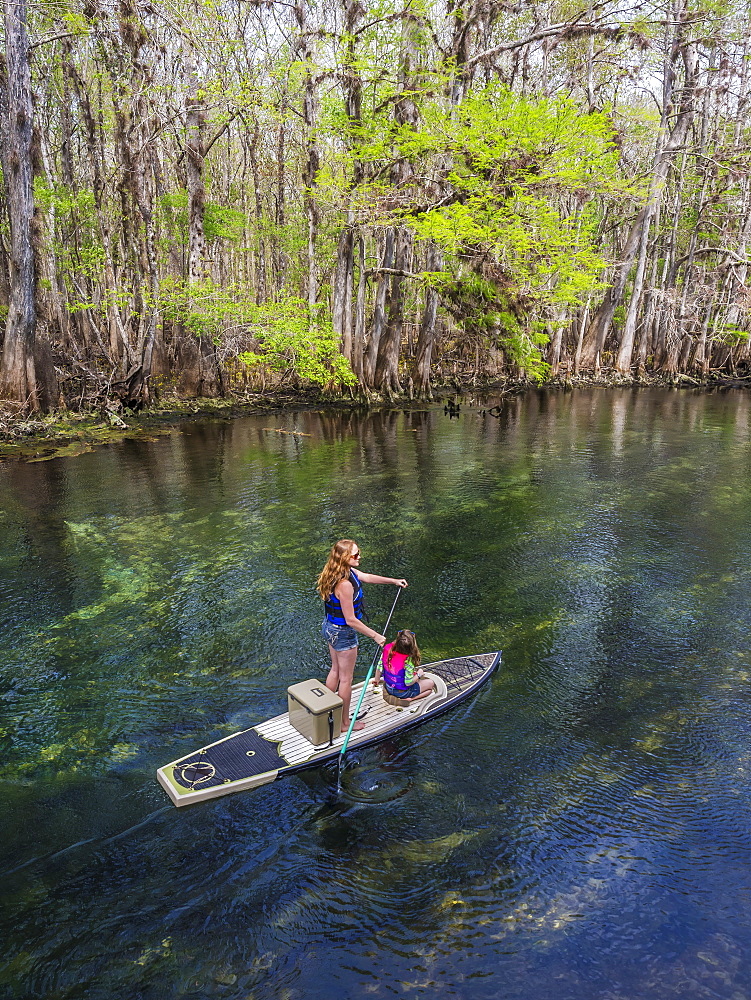 A mother and daughter paddleboard down the stream of freshwater spring, Chiefland, Florida, United States of America