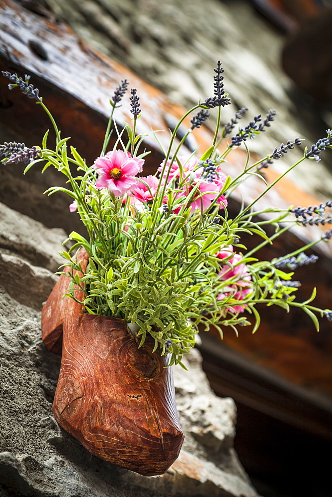 A wooden shoe carved flower pot along ancient cobblestone streets of Dolonne, near Courmayeur, Aosta Valley, Italy