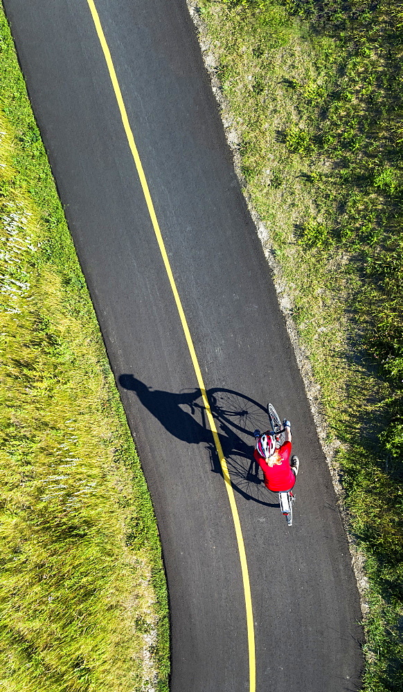 View from directly above a cyclist in a red shirt on a paved cycling trail, Calgary, Alberta, Canada