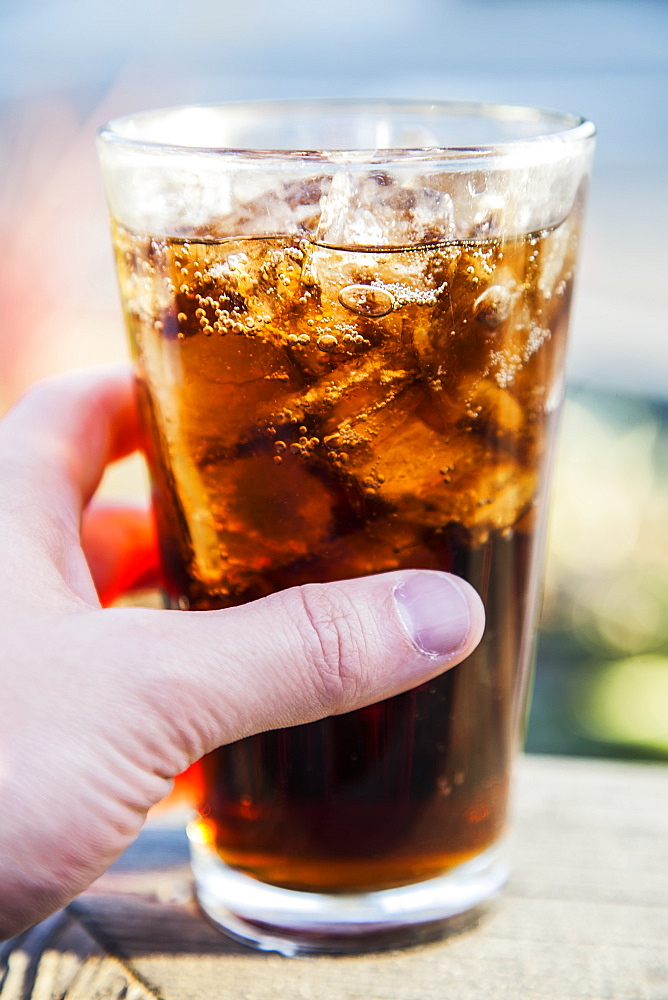 A hand holding a pint glass of cola with ice cubes, Long Beach, California, United States of America