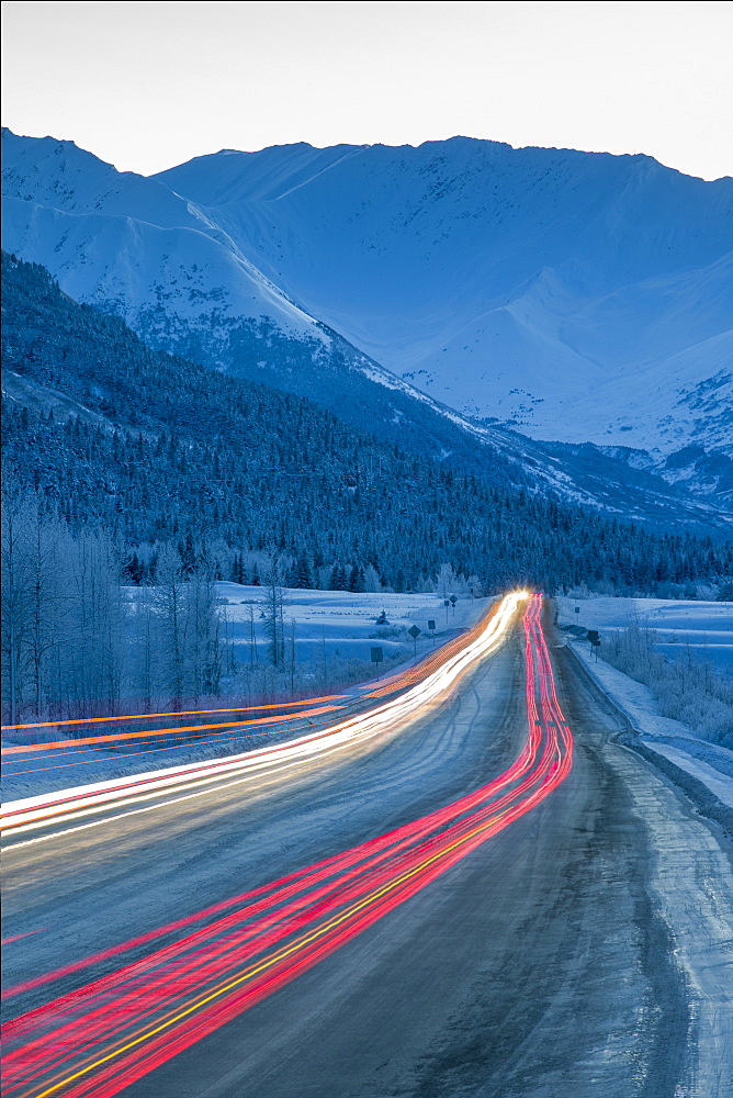 Car lights are blurred down the Seward Highway at dusk in winter, Turnagain Pass, Southcentral Alaska, USA