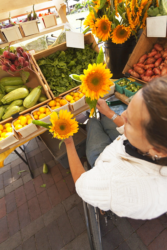 Woman with spinal cord injury sitting in a wheelchair shopping at outdoor market for sun flowers