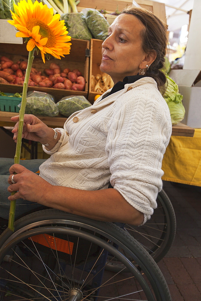 Woman with spinal cord injury sitting in a wheelchair shopping at outdoor market for sun flowers