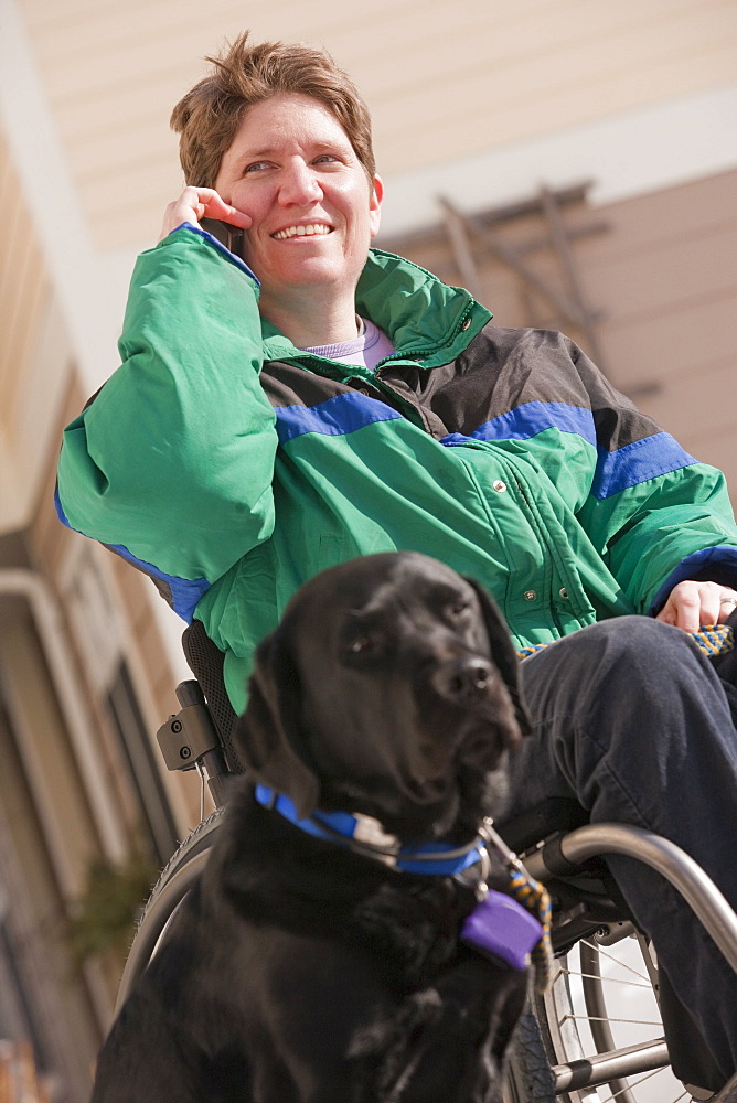 Woman with multiple sclerosis talking on a mobile phone with a service dog