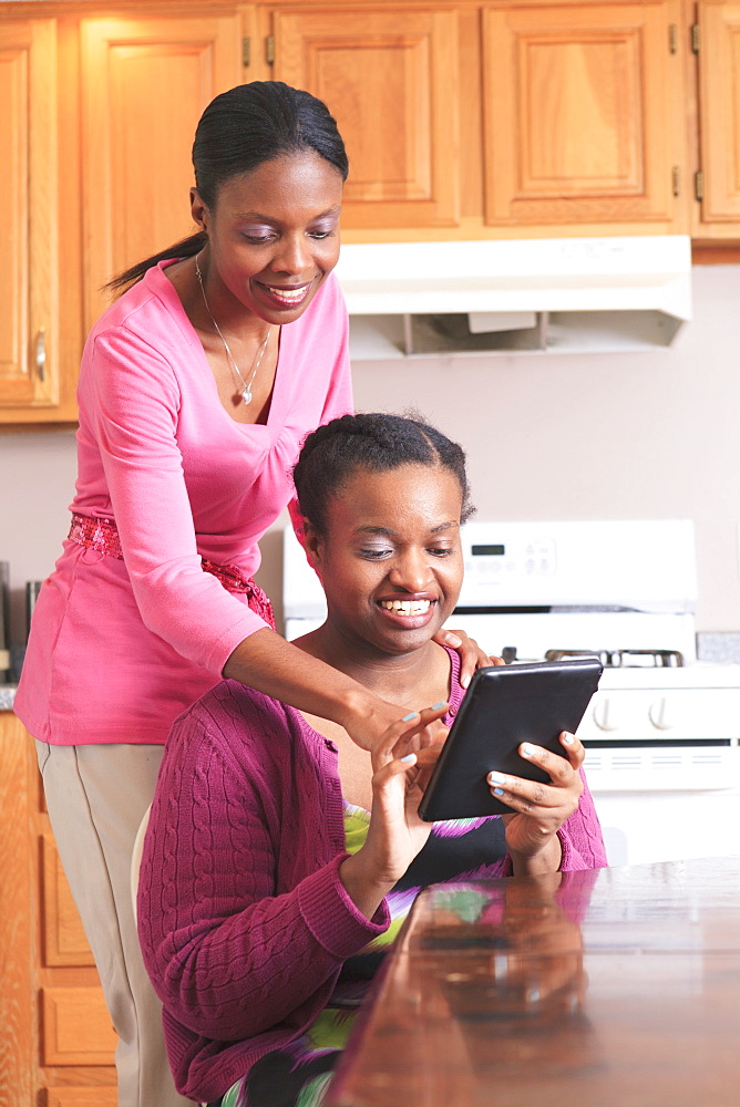 Two sisters looking at a digital tablet in the kitchen, one with learning disability