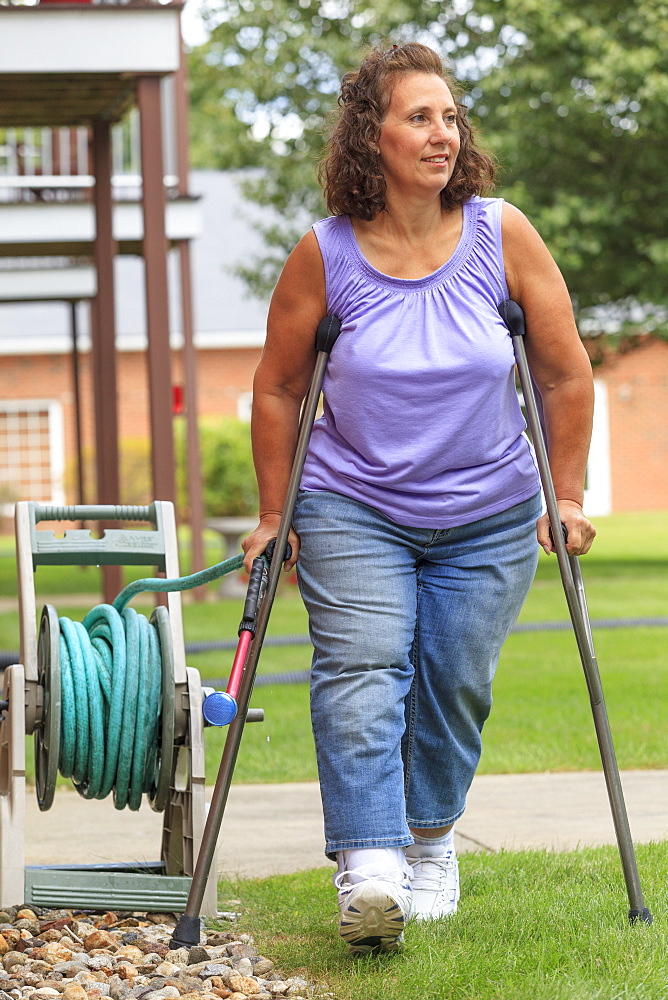 Woman with Spina Bifida walking with crutches and pulling garden hose