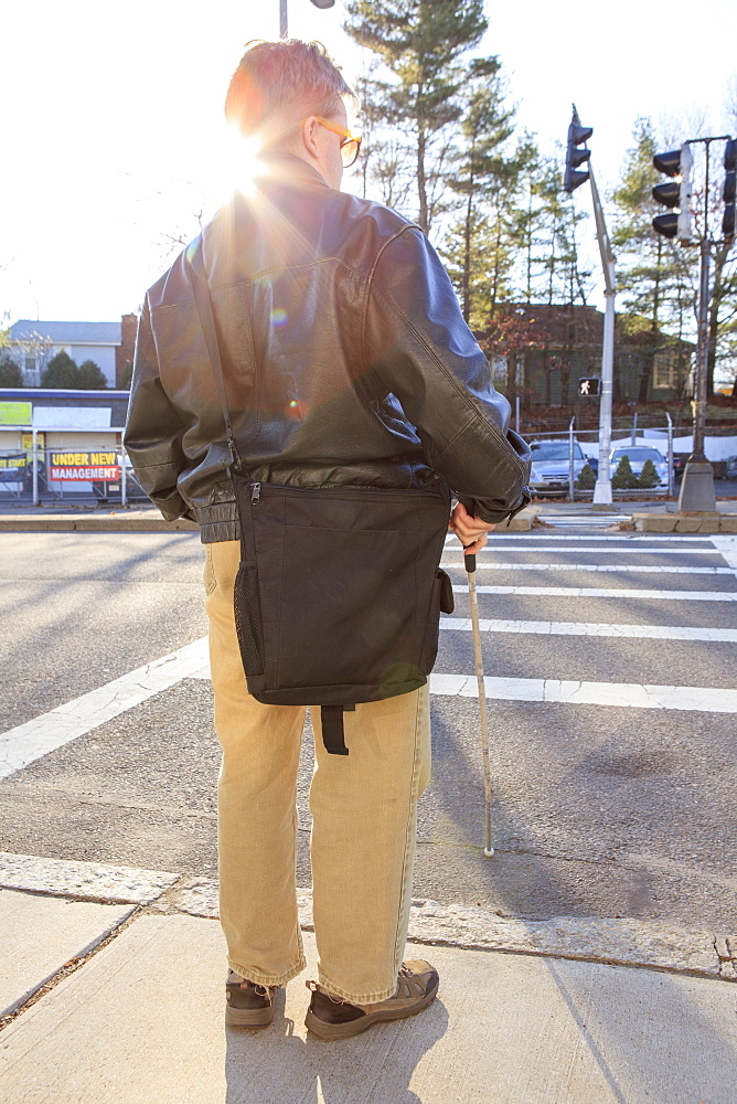 Man with congenital blindness about to cross the street using his cane