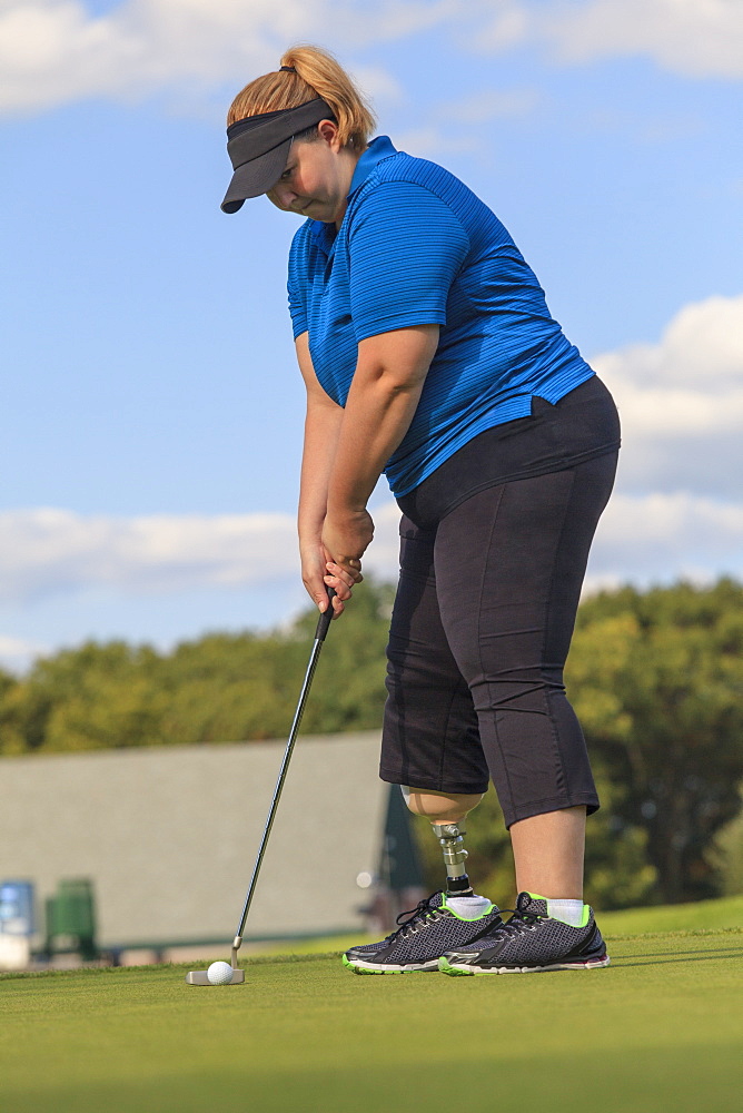 Woman with prosthetic leg at golf putting green