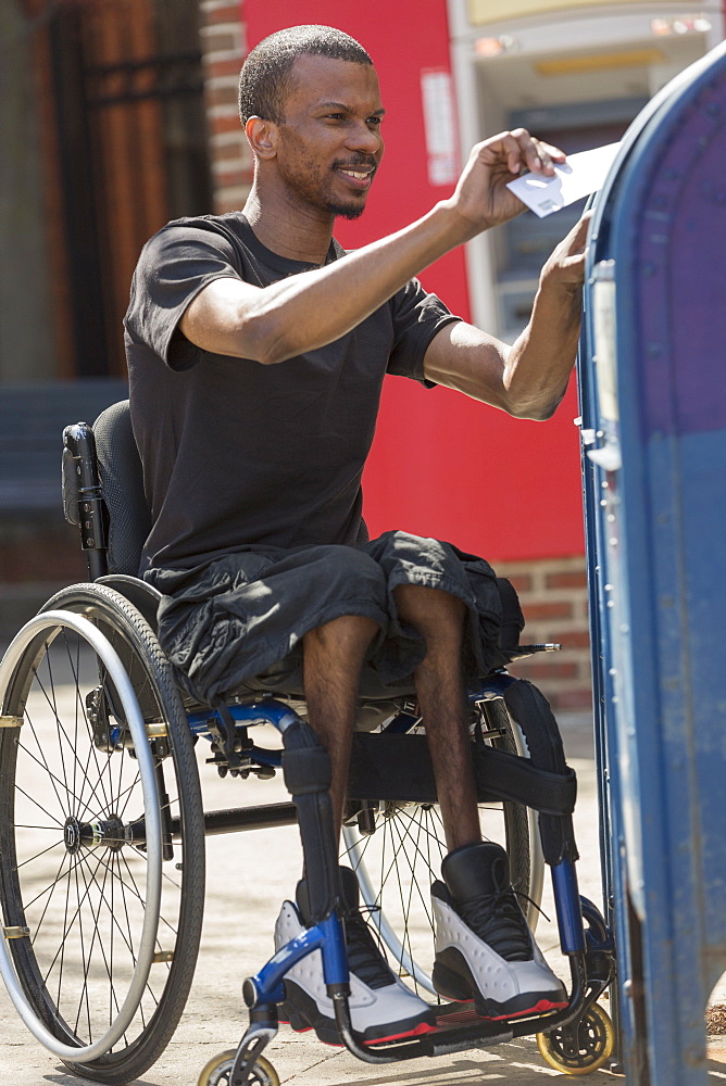 Man in a wheelchair who had Spinal Meningitis putting a letter in a public mail box