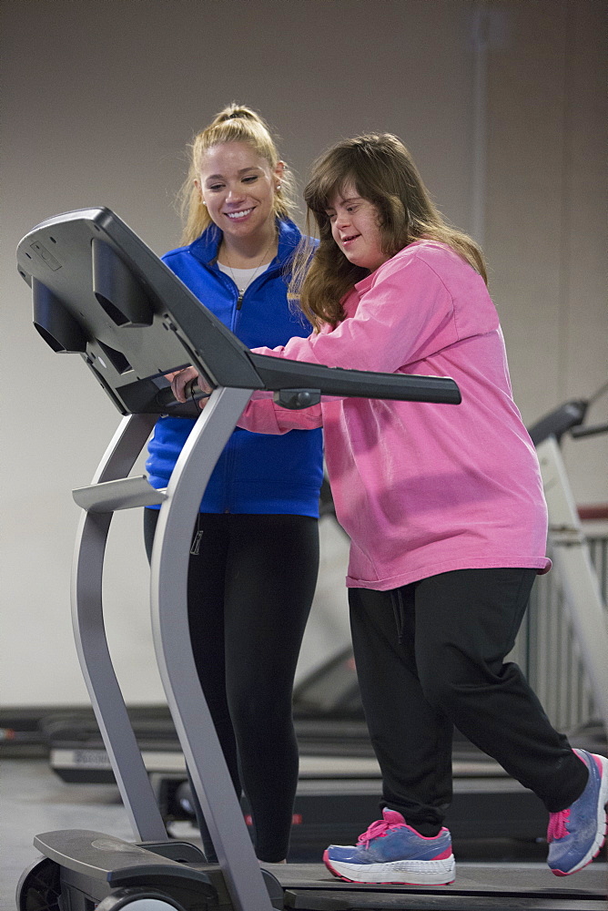 Young woman with Down Syndrome working out with her trainer on an exercise machine in gym