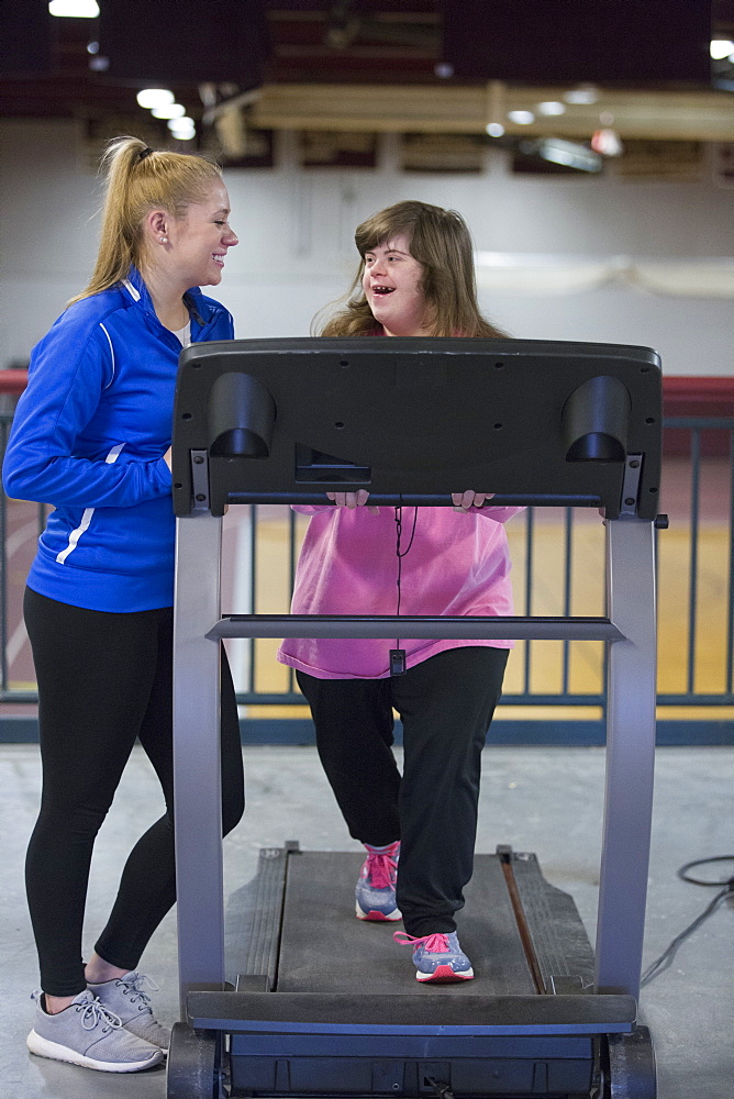 Young woman with Down Syndrome working out with her trainer on an exercise machine in gym