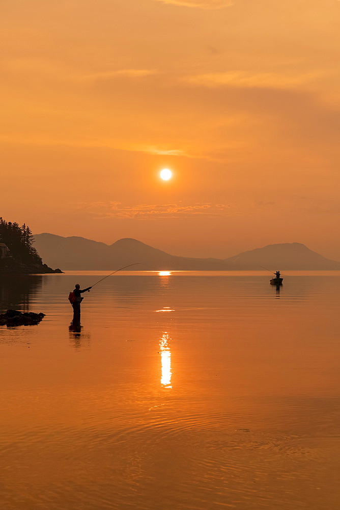 Silhouetted angler standing in the tranquil water fishing for king salmon at dusk; Alaska, United States of America