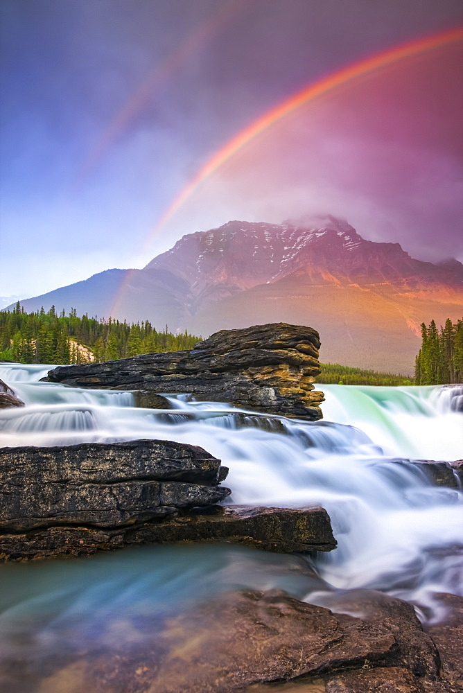 Double rainbow shining over a rugged waterfall and the Rocky Mountains, Jasper National Park; Alberta, Canada