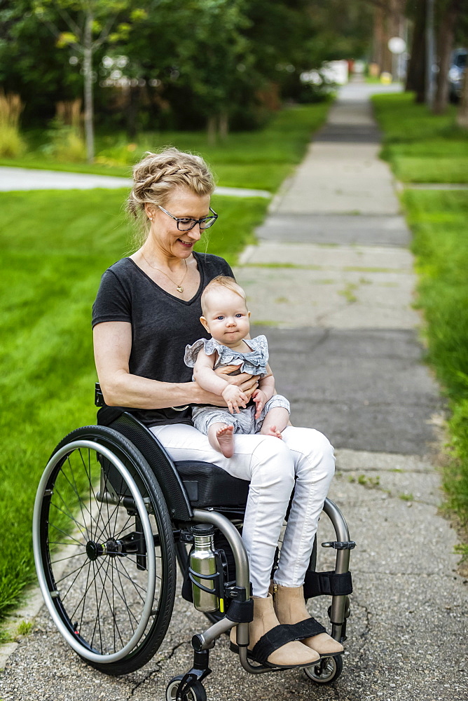 A paraplegic mom carrying her baby in her lap while using a wheelchair outdoors on a warm summer afternoon: Edmonton, Alberta, Canada