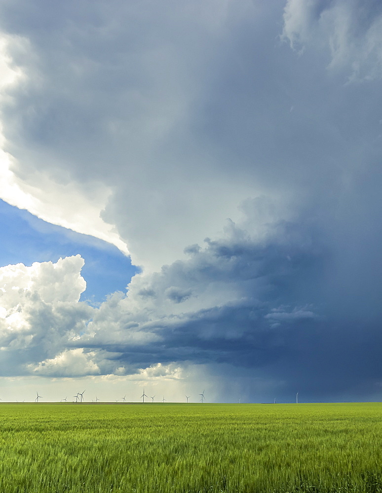 Storm cloud formations over farmland with a wind farm and turbines in the distance; United States of America