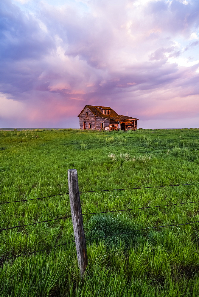 Abandoned barn on farmland with storm clouds glowing pink; Val Marie, Saskatchewan, Canada