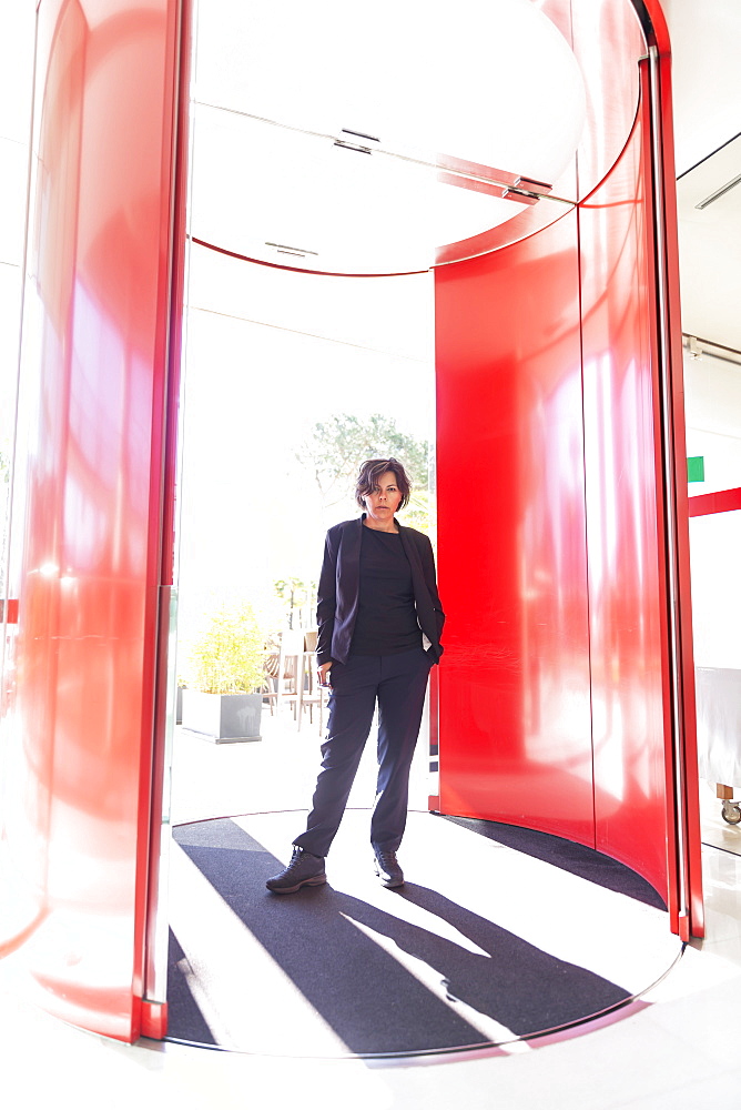 Woman standing in a red revolving doorway looking at the camera; Lugano, Ticino, Switzerland