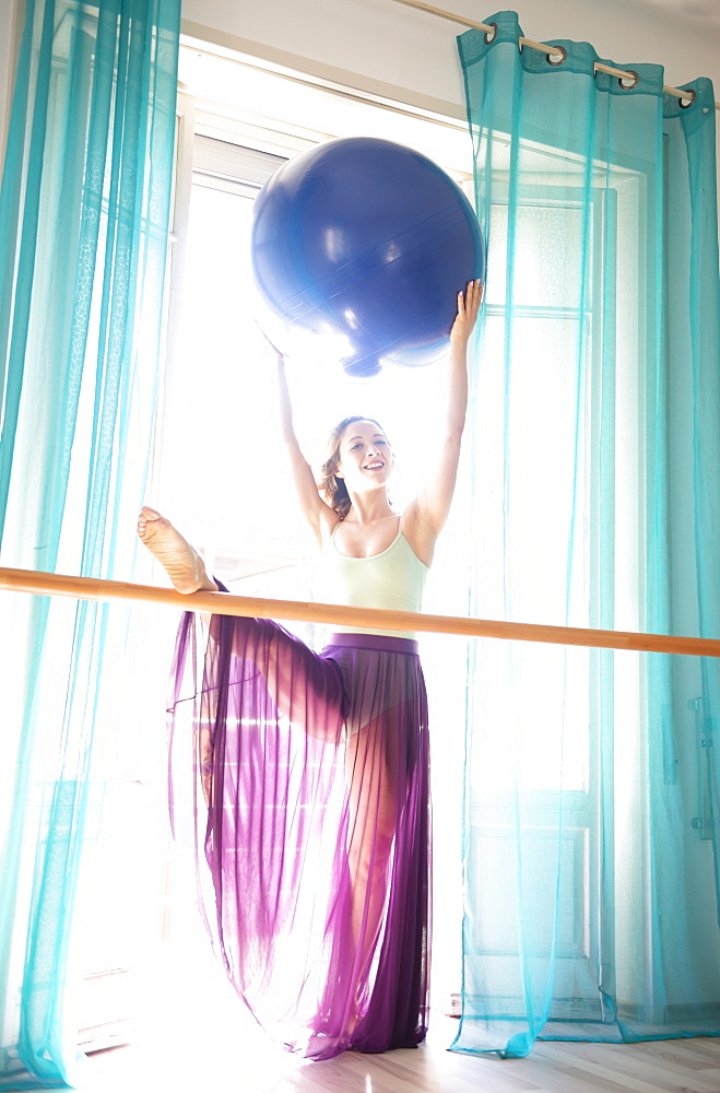 A female dancer stretches and practices in front of a window in a dance studio; Lugano, Ticino, Switzerland