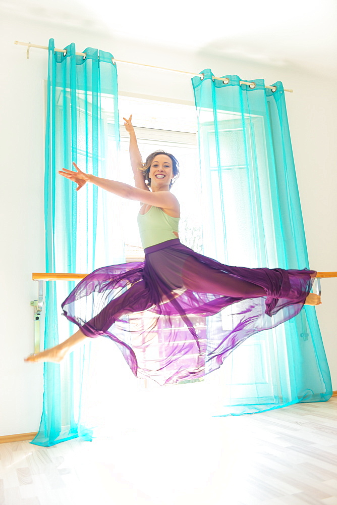 A female dancer leaps in mid-air in a dance move wearing a tulle skirt and looking at the camera; Lugano, Ticino, Switzerland